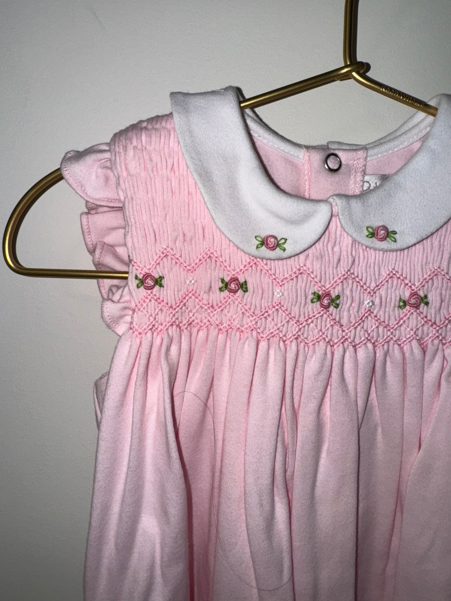 Pink smocked dress with floral embroidery on a hanger against a plain background.