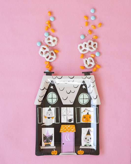 Halloween-themed house-shaped plate with candy on a pink background