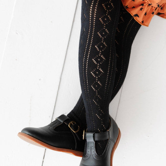 Black knee-high socks with white patterns worn with black shoes on a white background