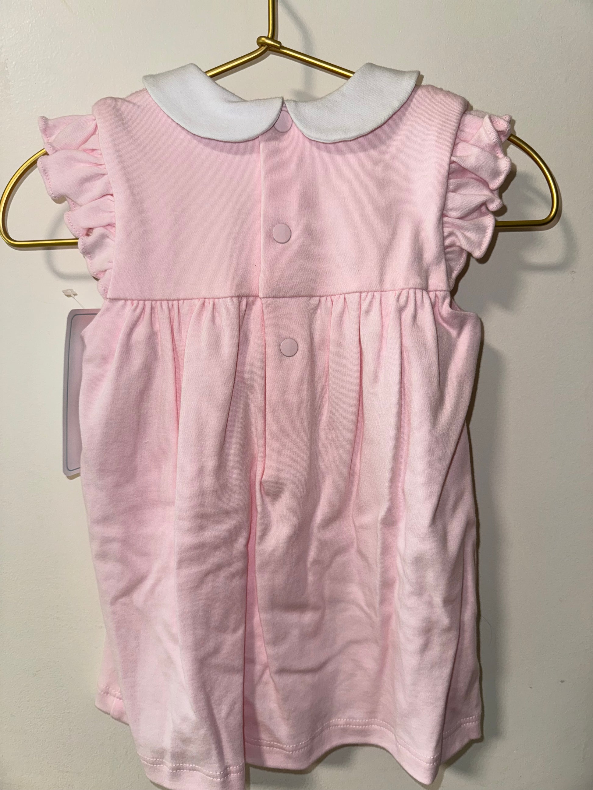 Pink dress with white trim on a hanger against a plain background