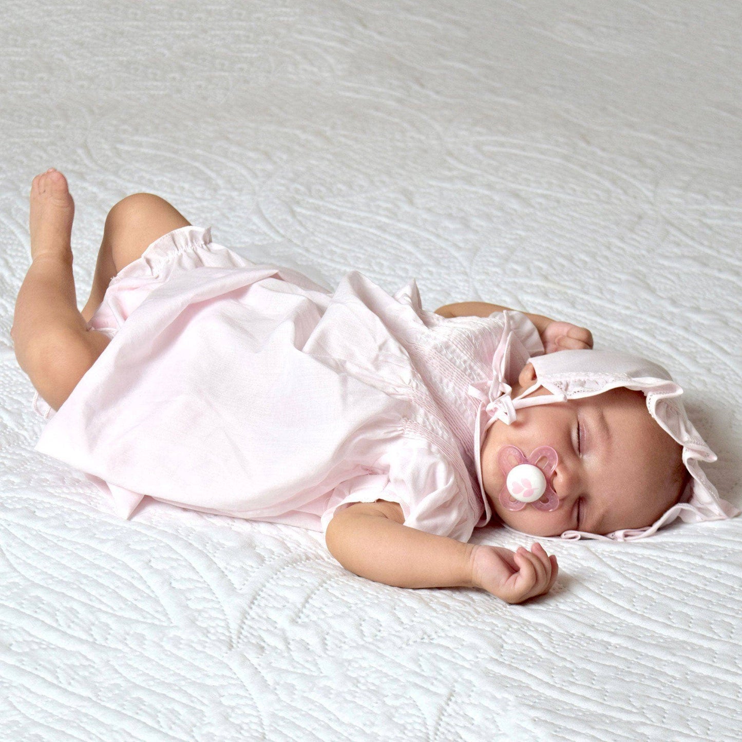 Baby in a pink outfit lying on a white surface