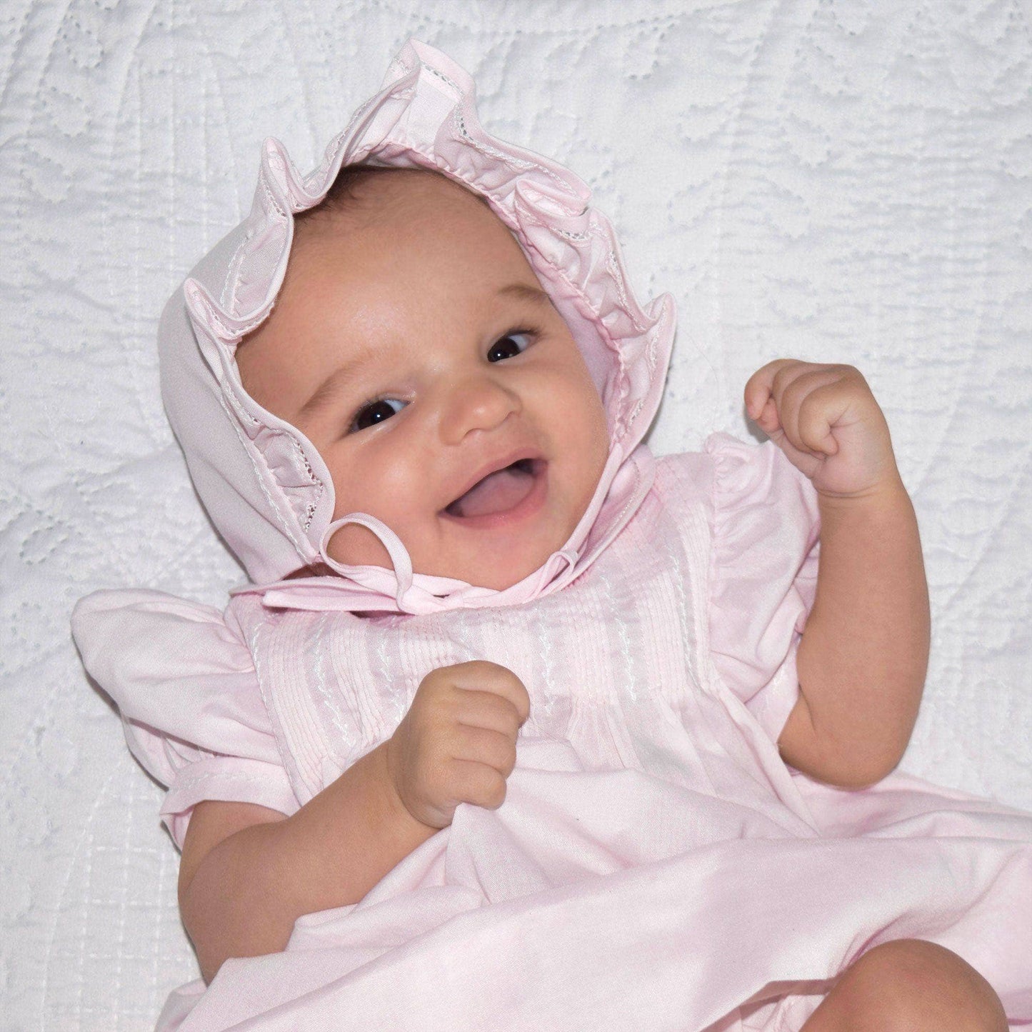 Baby wearing a pink bonnet and dress on a light gray background
